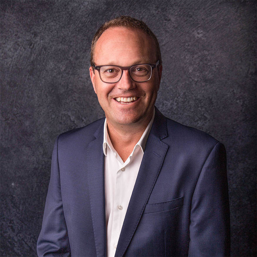 A man in glasses and a suit smiling at Capricorn Beach.