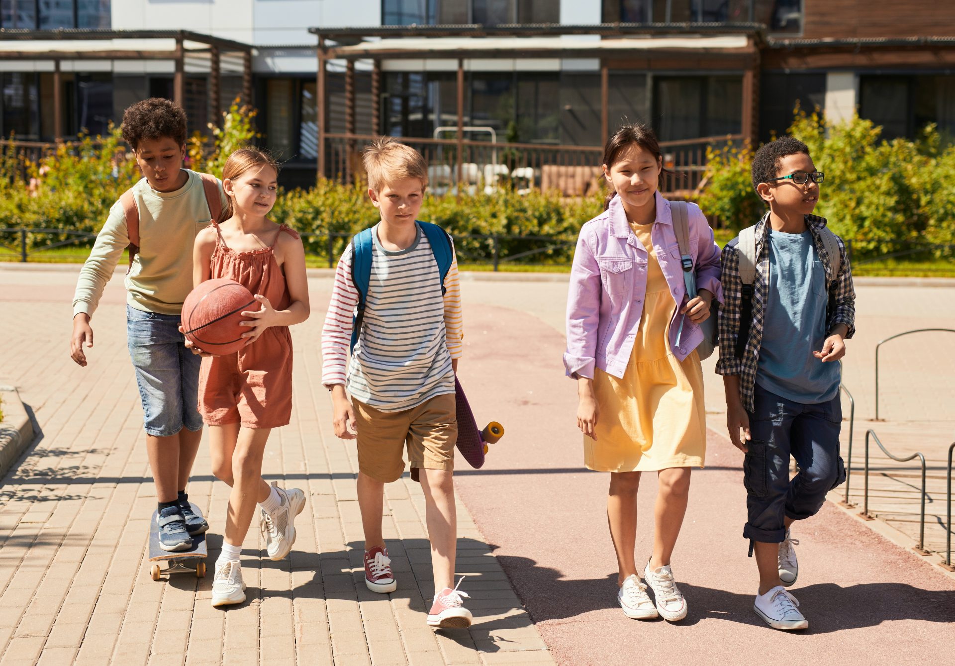 Group of children enjoying school holiday fun in Yanchep, walking with a basketball and skateboard on a sunny day