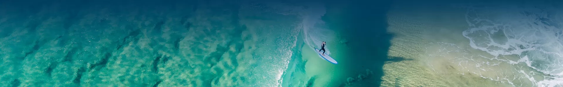 A surfer gracefully rides a wave at Capricorn Beach, captured from an aerial perspective.